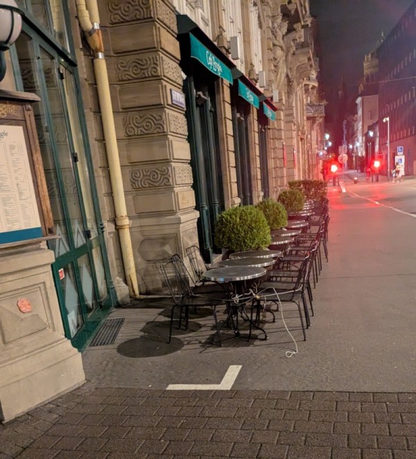 Chaises et tables alignés avec un câble antivol. Toutes les chaises qui font face à la façade sont en-dehors de la limite de la terrasse.
